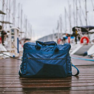 Eine gepackte Reisetasche steht auf einem Anlegeplatz für Segelboote
