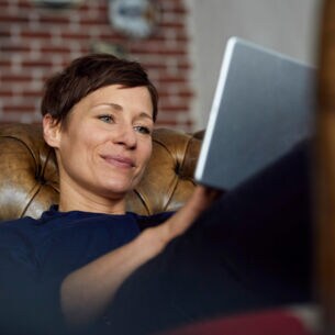 Eine Frau auf einer Ledercouch schaut zufrieden in ihr Tablet