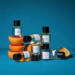 Sieben schlichte Parfümflakons sind vor blauem Hintergrund um Orangenhälften drapiert
