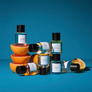 Sieben schlichte Parfümflakons sind vor blauem Hintergrund um Orangenhälften drapiert