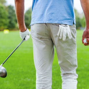Rückansicht eines männlichen Golfspielers, der mit Golfball und Driver in der Hand weggeht