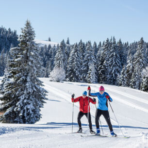 Zwei Skilanglaufende auf Loipe in hügeliger Winterlandschaft