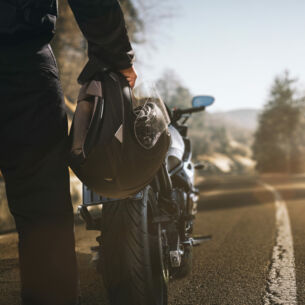 Ein Mann mit Motorradhelm in der Hand steht auf einer einsamen Landstraße vor einem Motorrad.