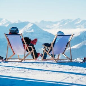 Zwei Menschen von hinten in einem Liegestuhl, sie blicken auf die verschneiten Berge des Skigebiets Wilder Kaiser