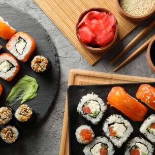Aufsicht unterschiedlicher Sushi-Sorten auf zwei Tellern, daneben Beilagen und Stäbchen