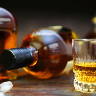Ein Glas mit Whisky vor einer stehenden und einer liegenden Flasche auf einem Tisch
