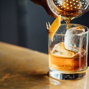 Ein Trinkglas mit Eis und Zitronenschale wird mit Whisky befüllt