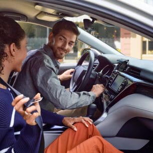 Ein junges Paar im Auto, auf dem Armaturenbrett ist Amazon Echo Auto verbaut.