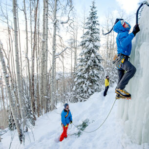 Ein Mann klettert am Eis, ein anderer sichert ihn von unten mit einem Seil