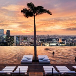 Ein endlos scheinender Pool mit Blick auf die Skyline Singapurs, mit Liegen und Palmen im Wasser