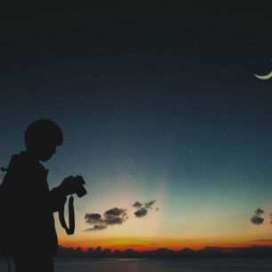 Ein Fotograf sieht in der Dunkelheit auf seine Kamera, am Himmel steht der Mond.