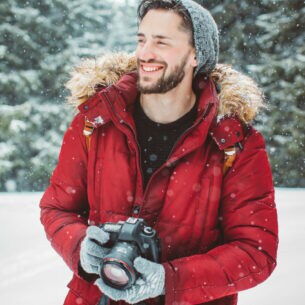 Ein Mann mit Kamera lächelt im Schnee.