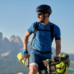 Mann in Sportoutfit auf dem Rennrad, im Hintergrund Berge