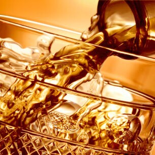 In ein Whiskyglas wird Flüssigkeit aus einem Flaschenhals gegossen, Nahaufnahme mit goldener Bildtonung