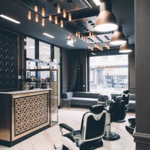 Das Interieur eines modernen Barbershops mit einem Messing verkleideten Tresen, Friseurstühlen aus Leder und einem dunkel gehaltenen cleanen Ambiente