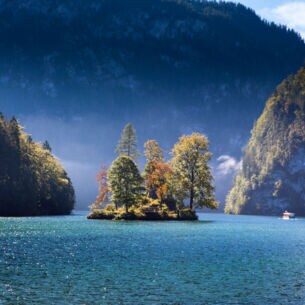 Ein großer See mit einer Insel mit herbstlichen Laubbäumen, eingebettet von riesigen Felswänden