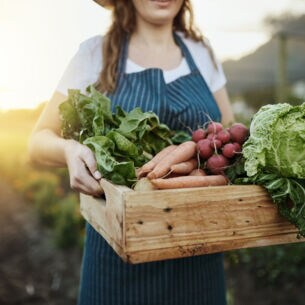 Eine junge Frau trägt eine Kiste mit frischem Gemüse.