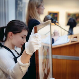 Eine Frau hält ein gerahmtes Bild während einer Auktion.