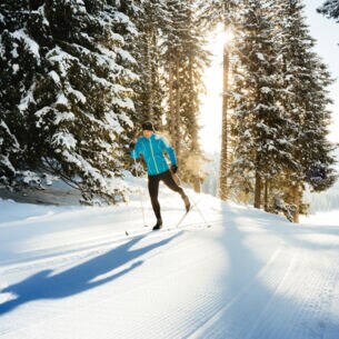 Ein Skilangläufer im klassischen Stil fährt durch den verschneiten Wald