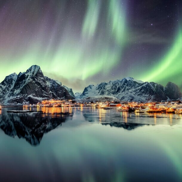 Schneebedeckte Berge und Wasser, darüber grün leuchtende Polarlichter
