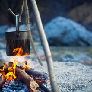 Ein Metalltopf hängt über einer Feuerstelle an einem See in der Dämmerung