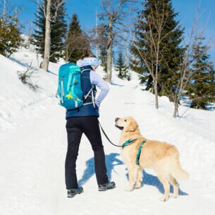 Frau mit Wanderrucksack und Hund im Schnee