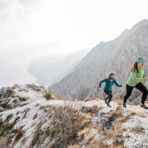 Zwei Läuferinnen sprinten bei kühler Witterung einen steilen und felsigen Fluss-Hang hinauf