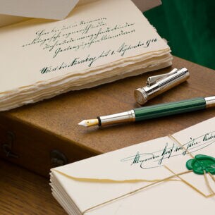Ein grün-silberner Füllfederhalter auf hölzernem Untergrun zwischen zwei nostalgischen Briefstapeln