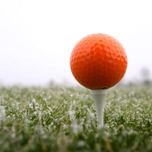 Ein roter Golfball auf dem Tee, darunter taubedeckter Rasen