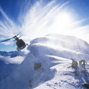 Ein Hubschrauber an einem verschneiten Berggipfel mit einer Personengruppe mit Snowboards