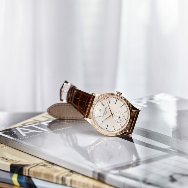 Eine klassische Herrenuhr von Patek Philippe mit braunem Lederarmband, goldener Lünette und hellem Zifferblatt auf Hochglanzmagazinen