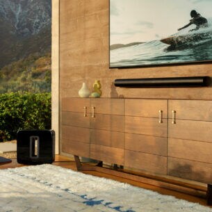 Ein modernes Wohnzimmer mit Panoramafenster sowie einem TV-Gerät und einer Soundbar an der Wand, daneben ein Subwoofer auf dem Boden