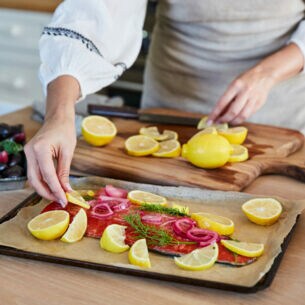 Eine Frau bereitet Lachs mit Zitronenscheiben auf einem Blech in einer Küche zu