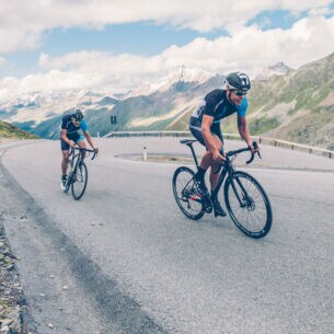 Zwei Rennradfahrer auf einer Bergstraße.