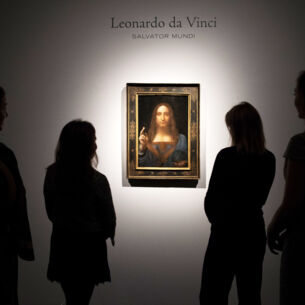 Rückansicht mehrerer Personen als Silhouetten, die Leonardo da Vincis Gemälde Salvator Mundi in einem goldenen Rahmen an einer weißen Wand betrachten