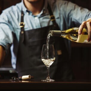 Ein Mann mit Schürze gießt Weißwein in ein Glas