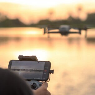 Rückansicht einer Person, die mit einer Drohne per Smartphone einen See fotografiert.