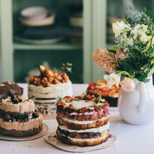 Fünf hausgemachte, stilvoll dekorierte Torten stehen auf einem Küchentisch neben einem Blumenstrauß