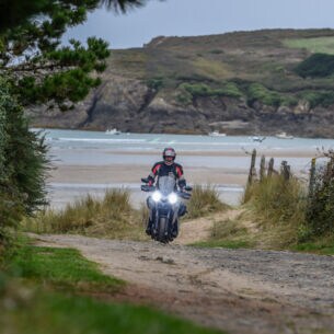 Ein Motorradfahrer auf einem Schotterweg an einer rauen Küste