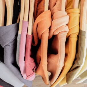 Eine Reihe Sweatshirts in bunten Pastellfarben auf Kleiderbügeln aus Holz