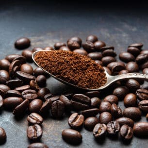 Ein Löffel mit Kaffeepulver liegt auf mehreren Kaffeebohnen.