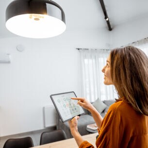 Eine Frau steuert über ihr Tablet die Wohnzimmerlampe