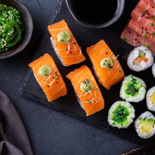 Veganes Sushi auf einer Schieferplatte angerichtet mit Sojasoße und Algensalat