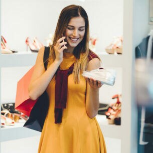 Eine junge Frau betrachtet in einer Modeboutique einen weißen Sneaker in ihrer Hand, während sie telefoniert