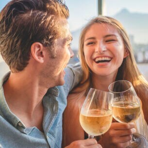 Ein Paar sitzt lachend nebeneinander und stößt mit Weingläsern an