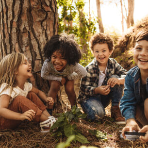 Vier fröhliche Kinder sitzen vor einem Baum im Grünen