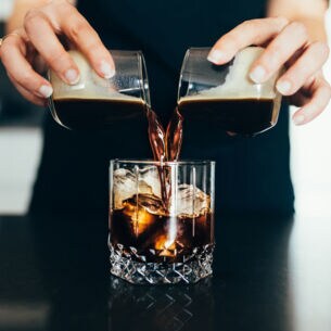 Eine Frau gießt kalten Kaffee in ein Glas mit Eiswürfeln