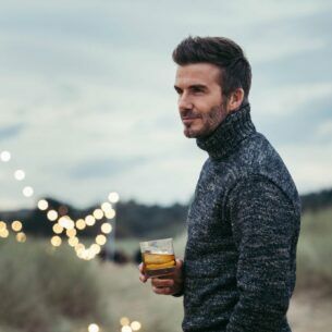 Porträtaufnahme von David Beckham in den Dünen mit einem Glas Whisky in seiner Hand