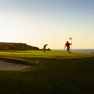 Zwei Golfspieler beim Abschlag auf einer Golfanlage im Sonnenuntergang