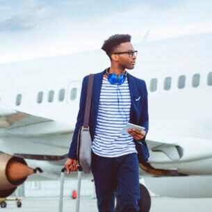 Ein junger, stylisher Geschäftsmann mit Reisegepäck vor einem Flugzeug